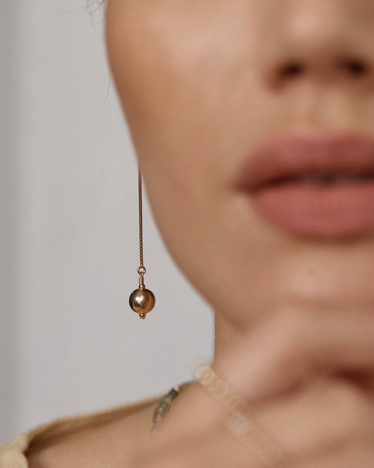 Close-up of a person wearing a gold dangling earring with a blurred background