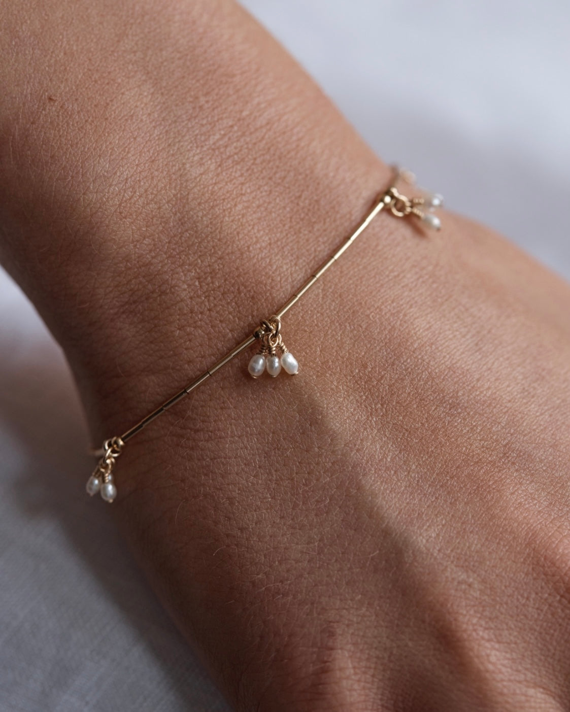 Gold bracelet with pearl beads on a wrist against a neutral background