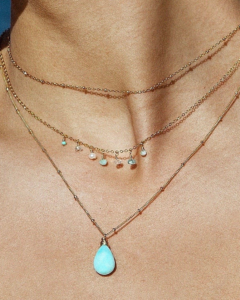 Layered necklaces with a blue peruvian opal gemstone pendant on a person's neck
