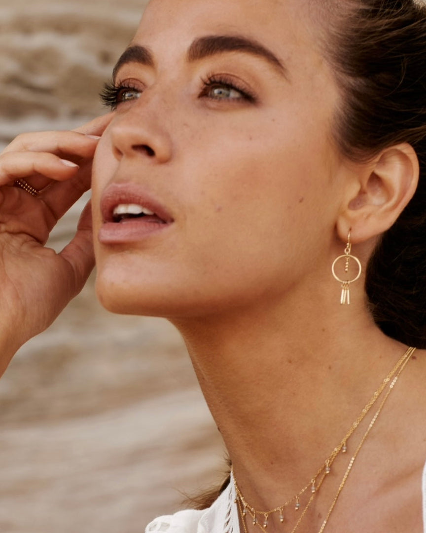 Woman wearing gold earrings and necklaces with a blurred natural background