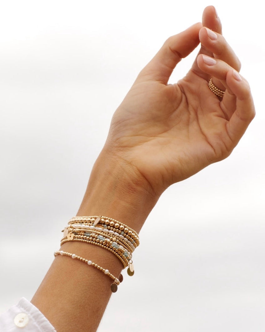 Hand wearing multiple gold bracelets on a white background