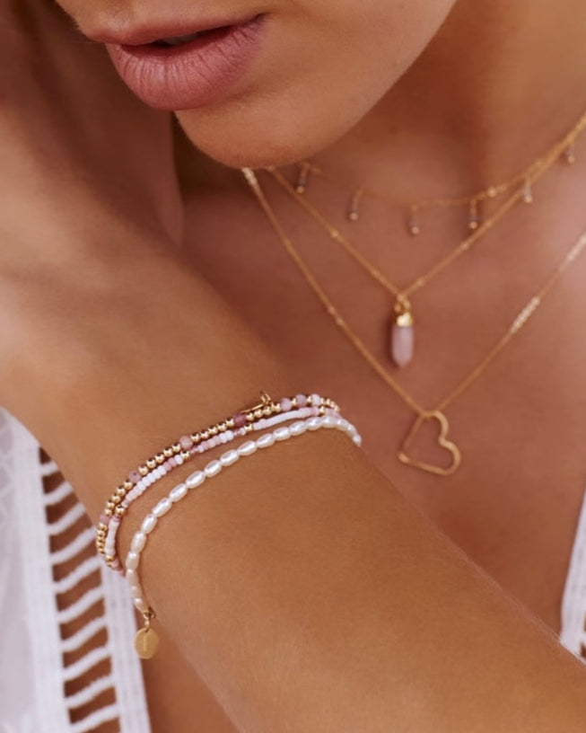 Close-up of a person wearing gold necklaces and bracelets on a blurred background