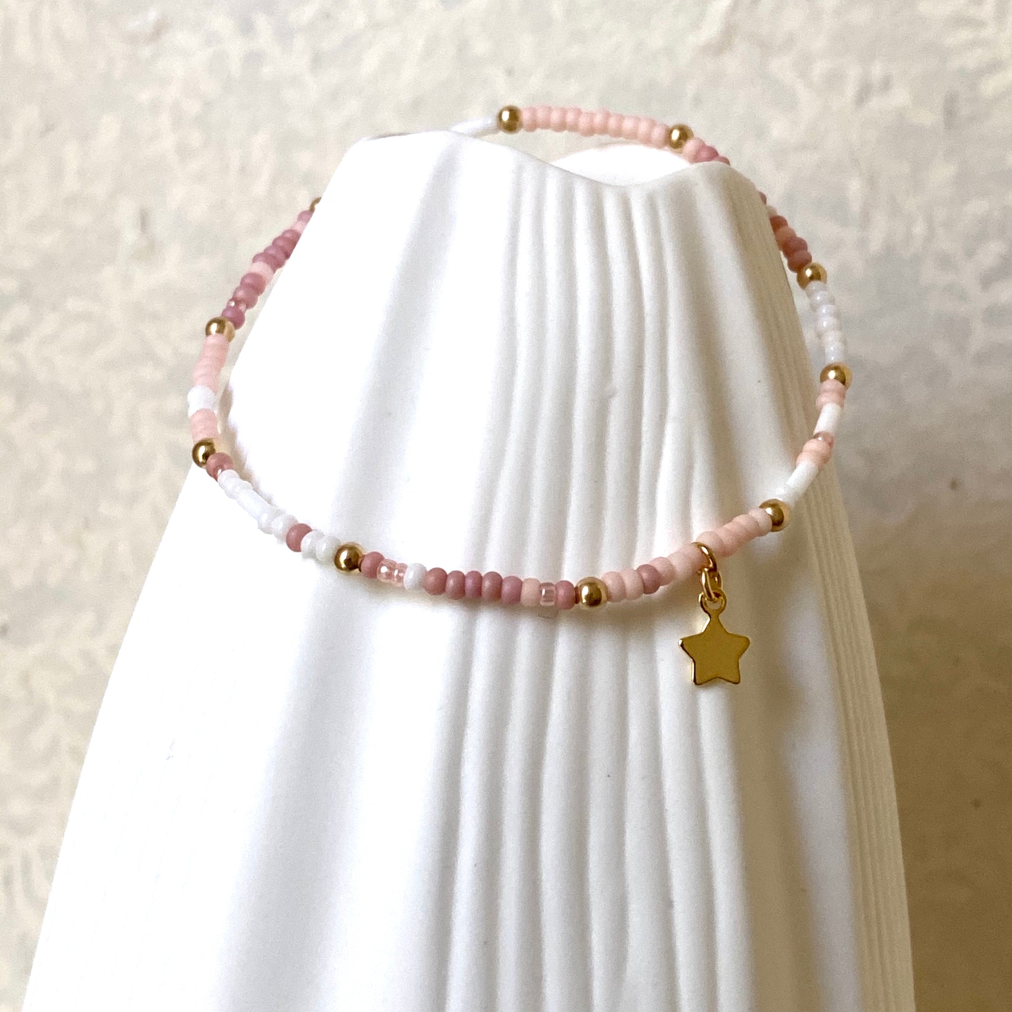 Pink white and gold beaded bracelet on white jewellery stand.