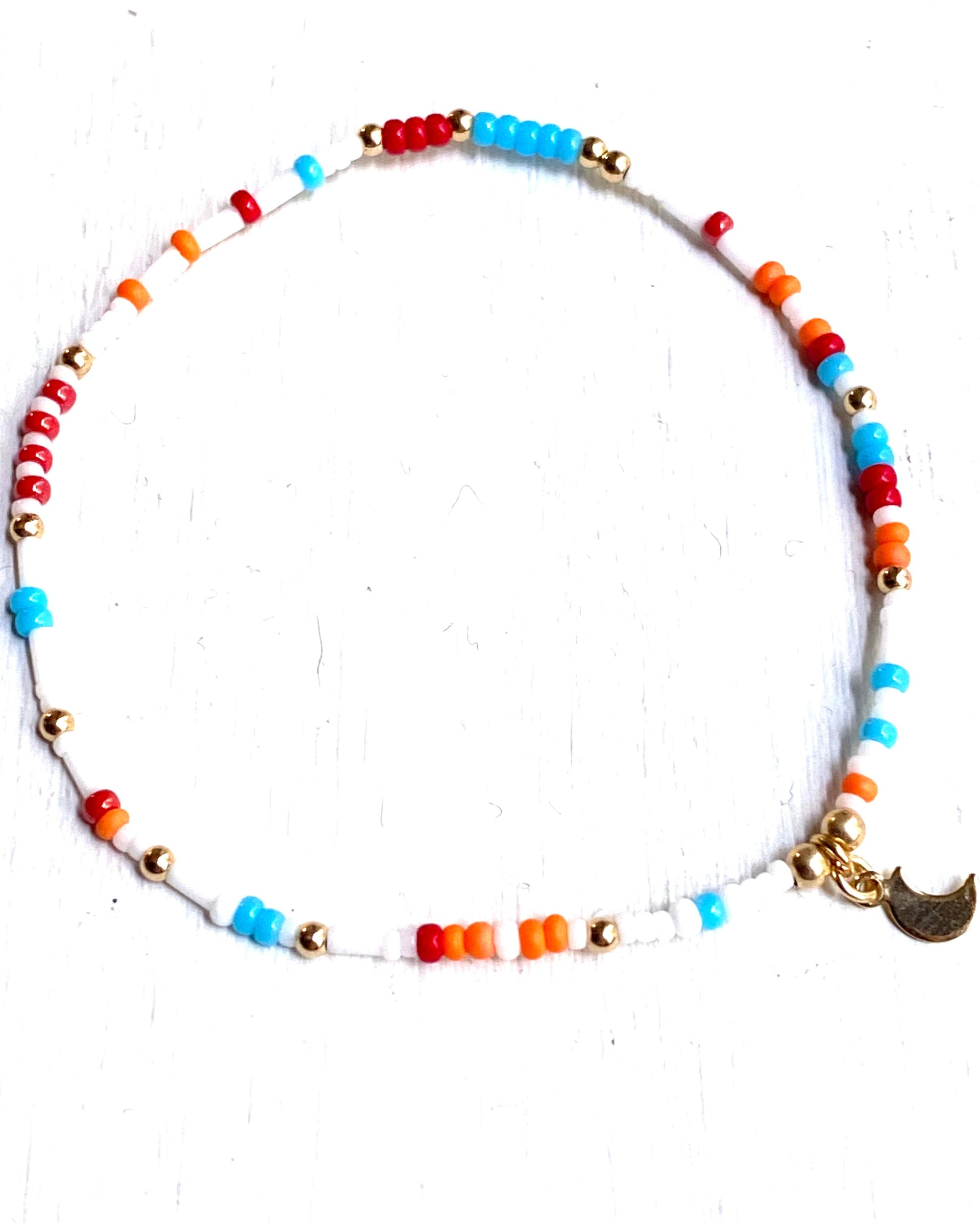 A colorful bracelet with a mix of white, turquoise, orange, and red tiny glass beads, 14Kt Gold Filled beads, and a gold filled moon charm on a stretch cord.