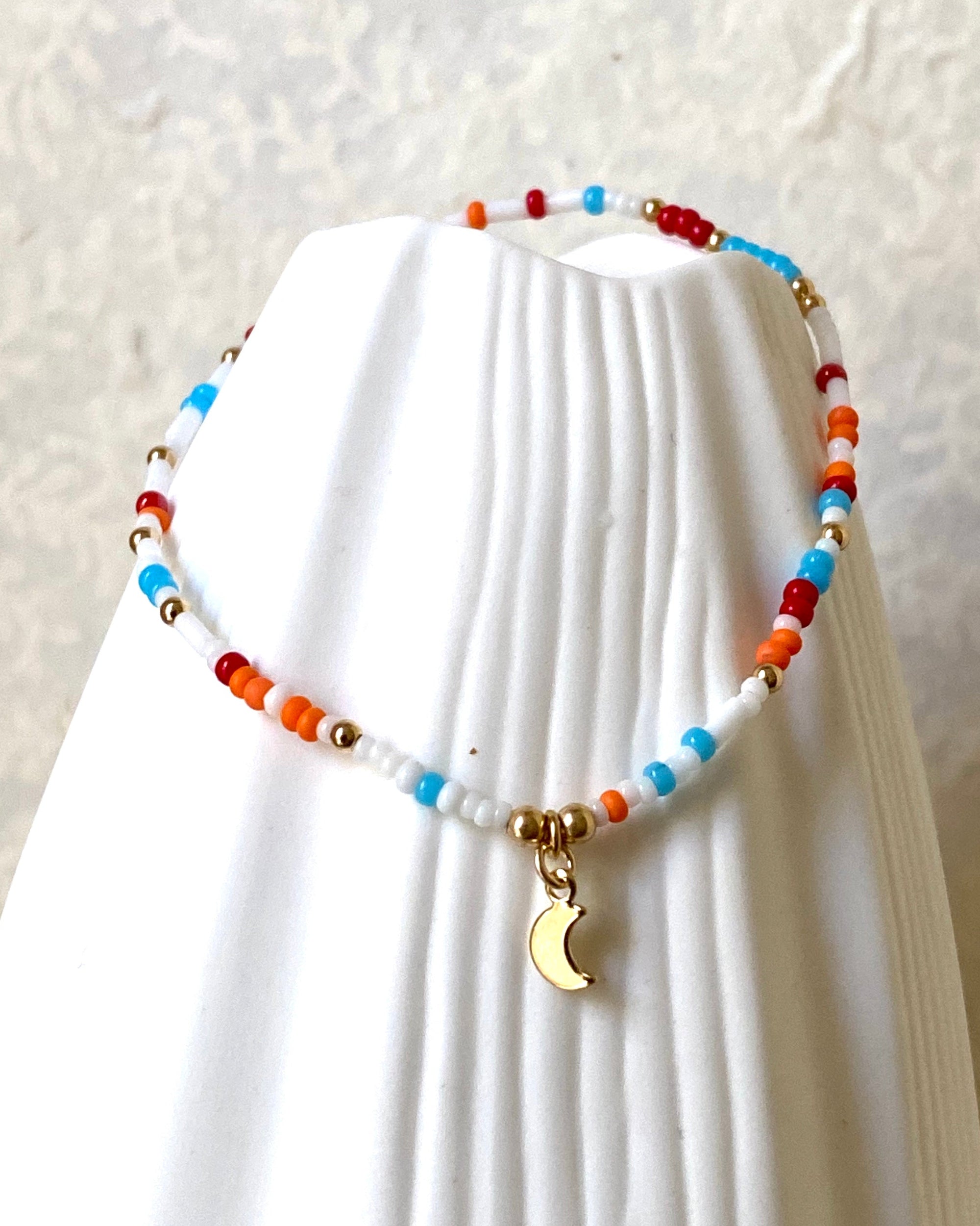 Colorful beaded necklace with a moon charm on a white jewellery stand.