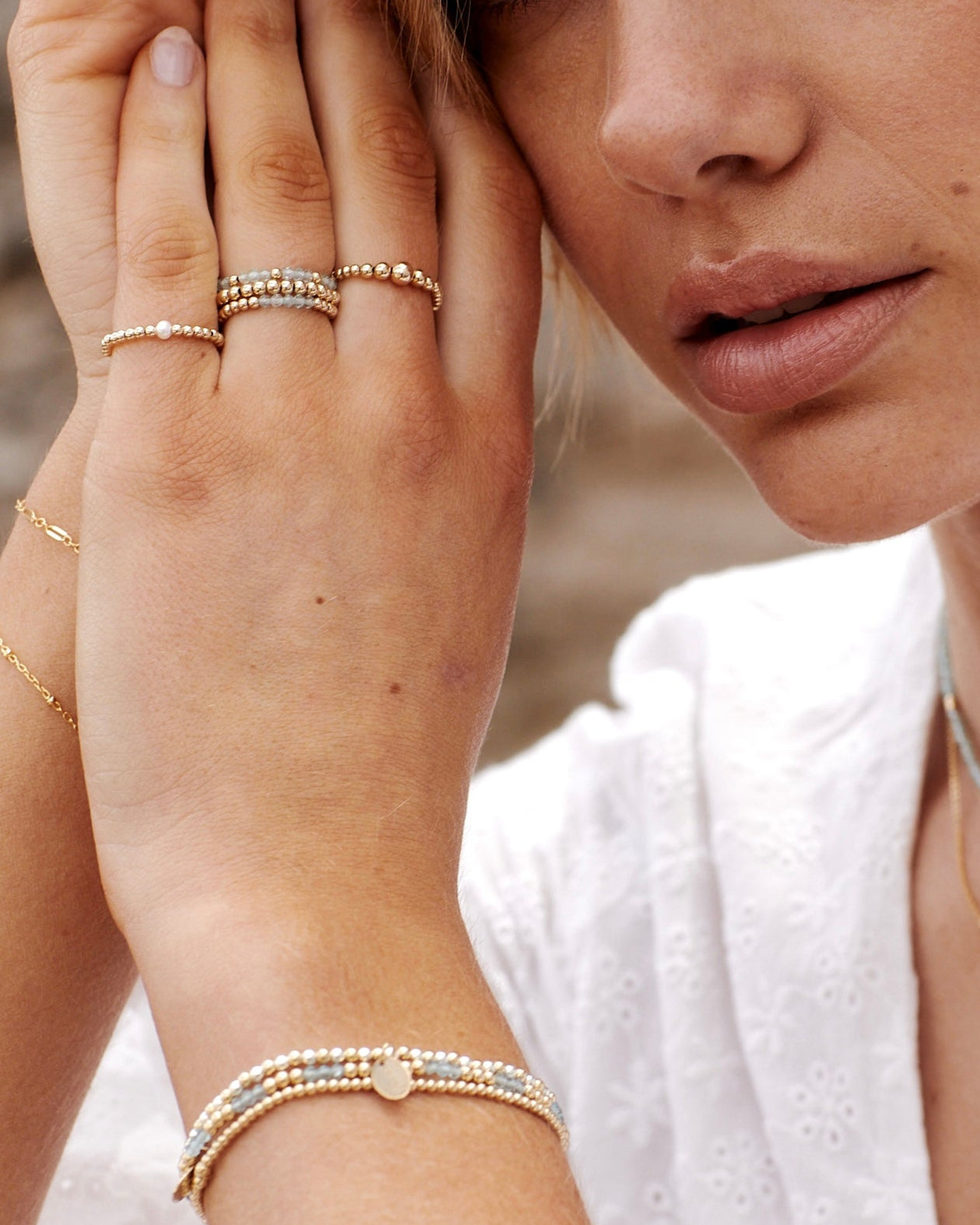 Close-up of a woman's hand wearing multiple gold rings and bracelets against a blurred background.