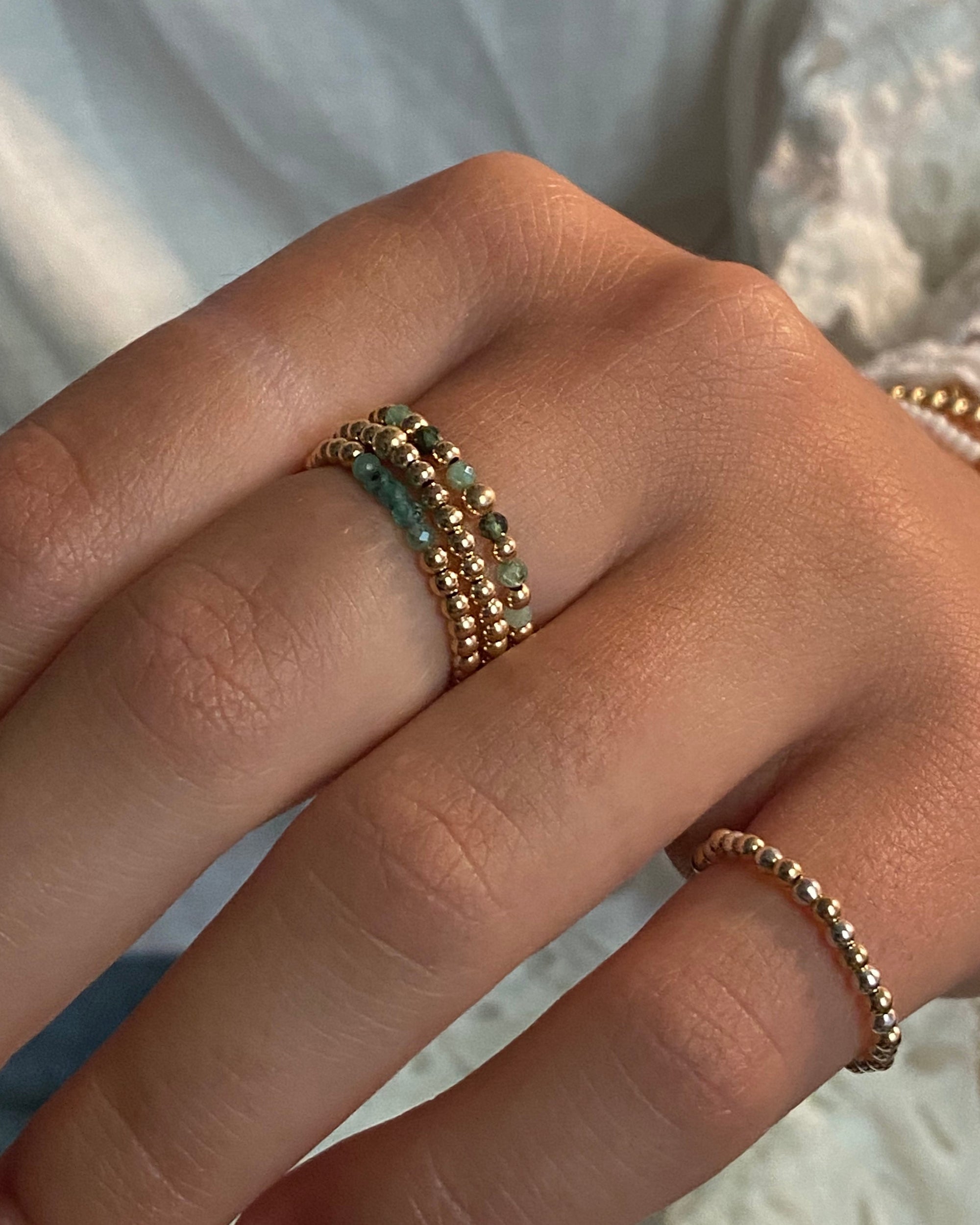 Close-up of a hand wearing multiple gold rings with emerald gemstones on a neutral background