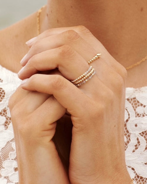 Close-up of hands wearing labradorite gemstone gold rings with a blurred background