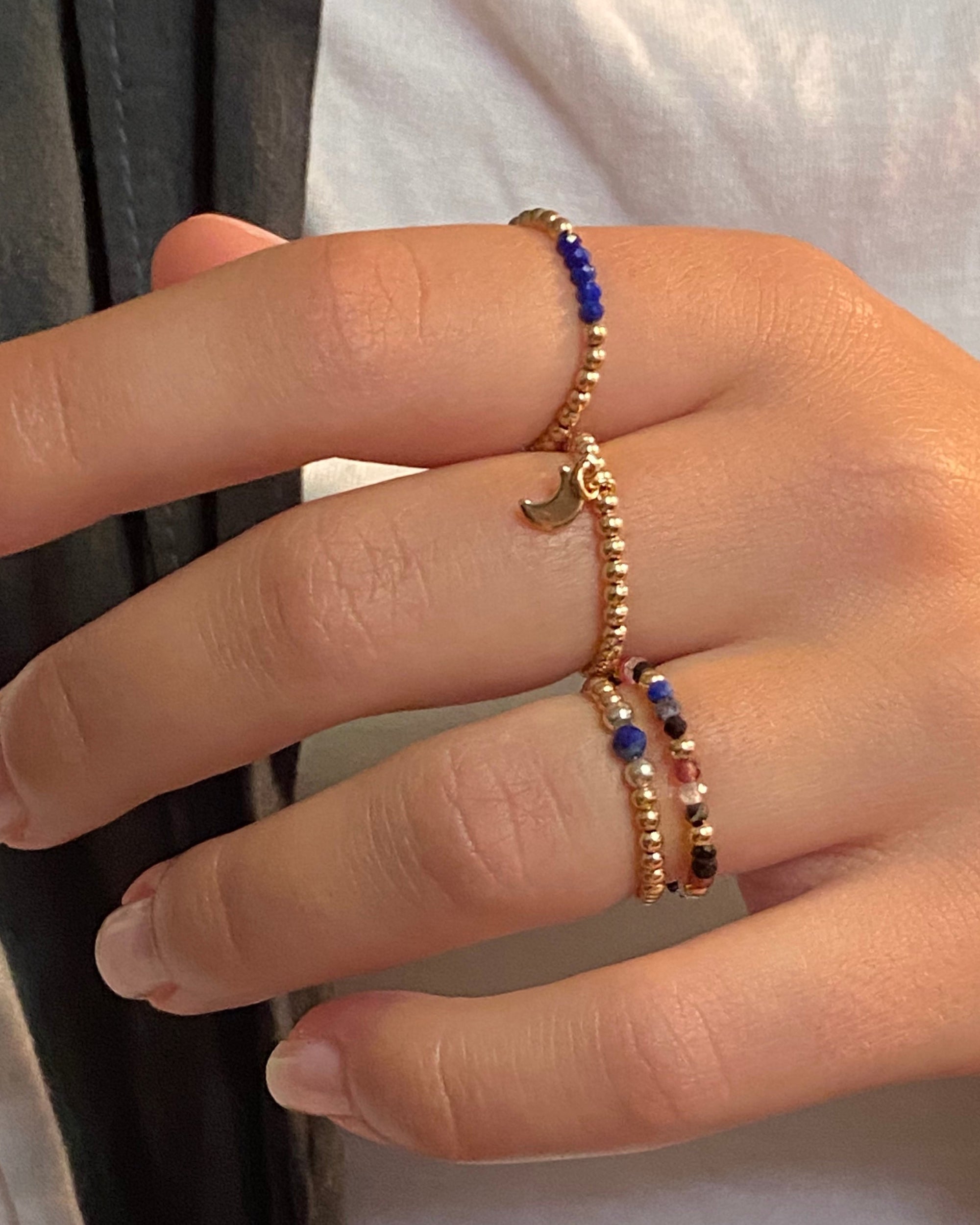 Close-up of a hand wearing gold and lapis lazuli gemstone rings.