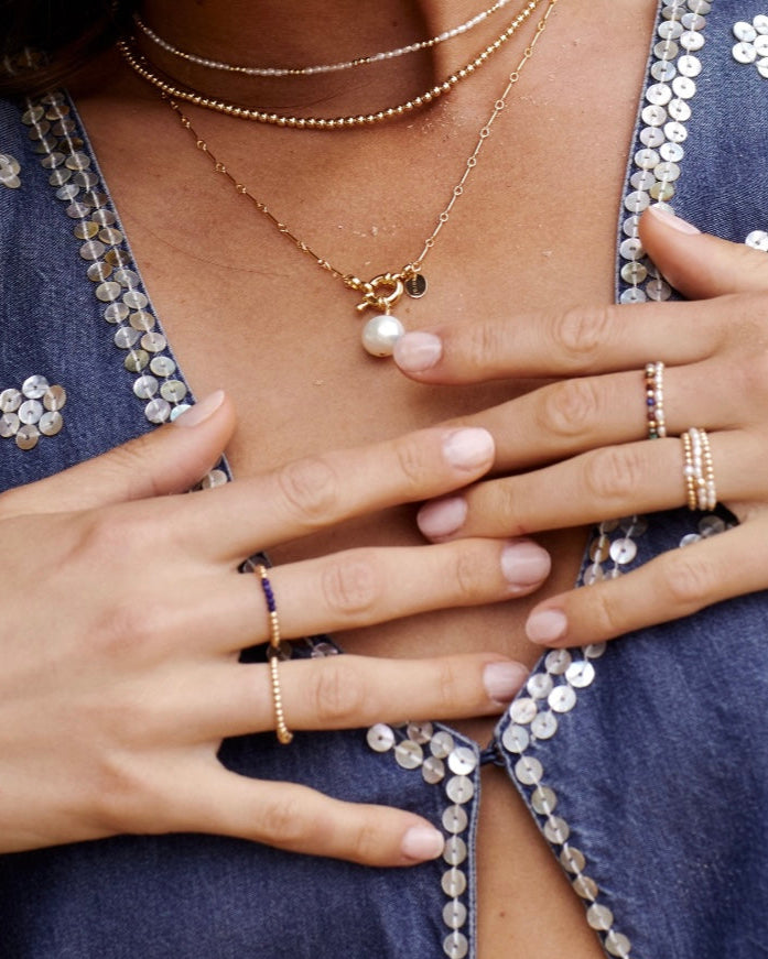 Close-up of model wearing multiple necklaces with pearls rings with both pearls and lapis lazuli gemstones.