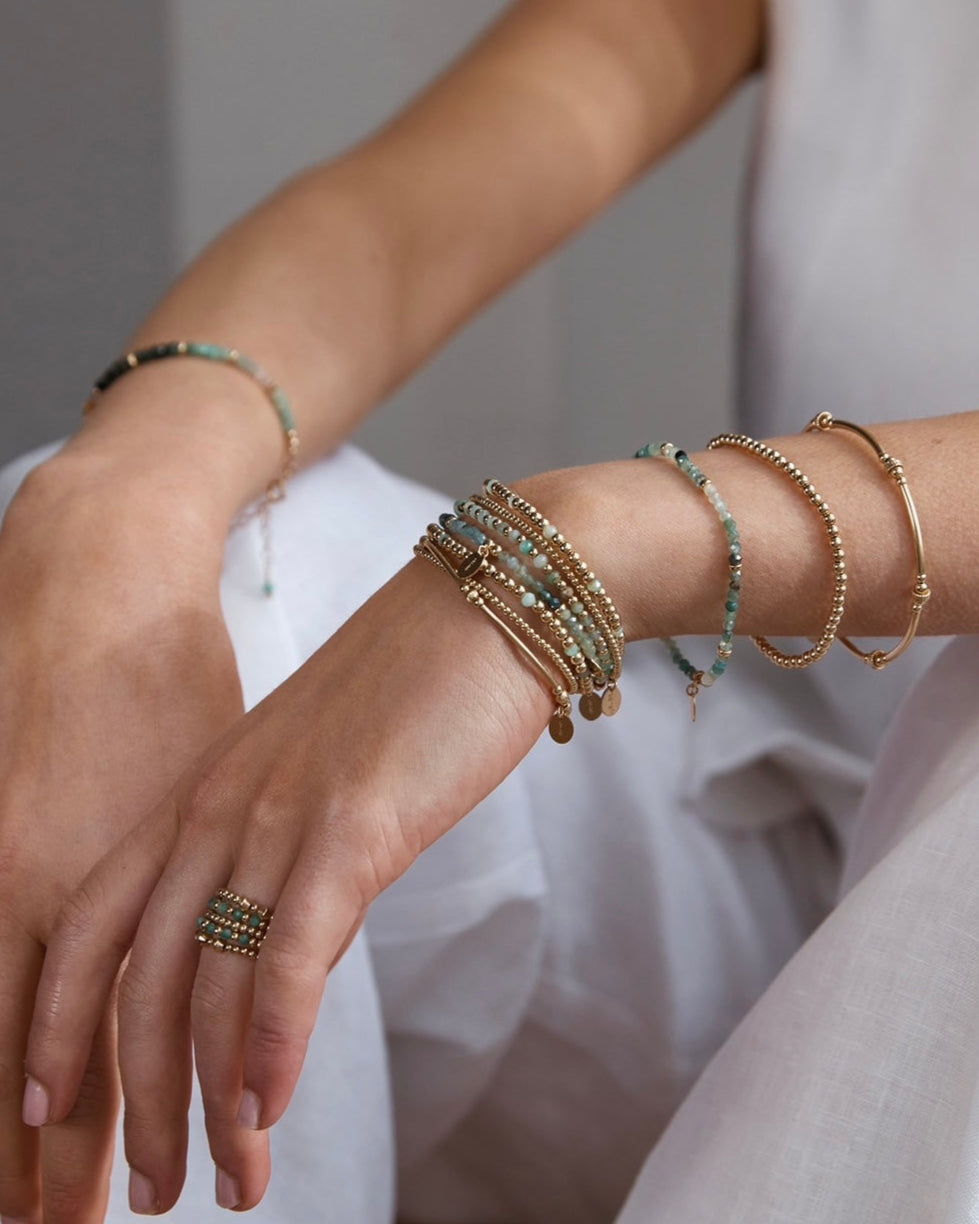 Close-up of a model's wrist with multiple bracelets featuring grandidierite, emerald and chrysoprase gemstones on a neutral background