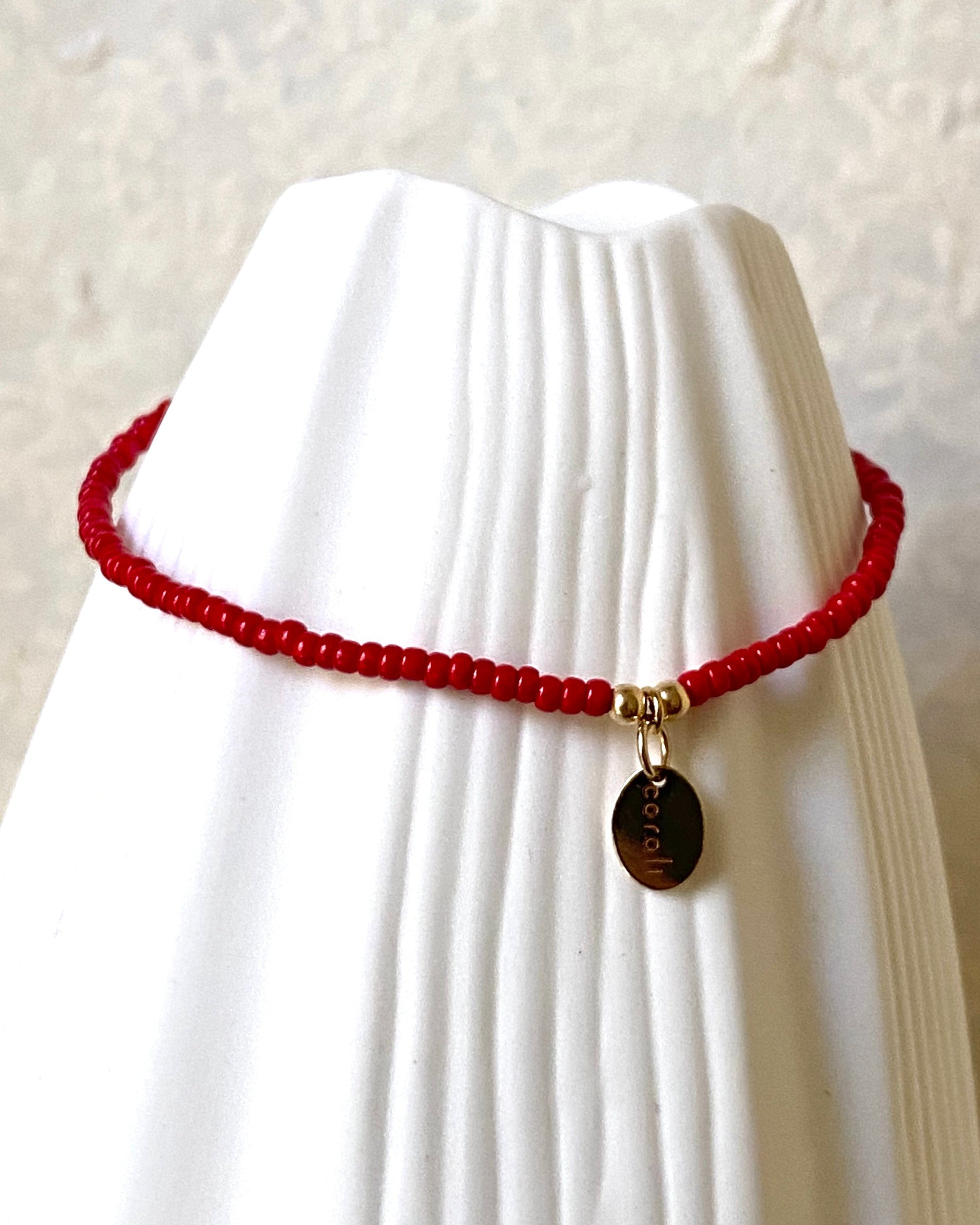 Red beaded bracelet on a white vase against a beige background