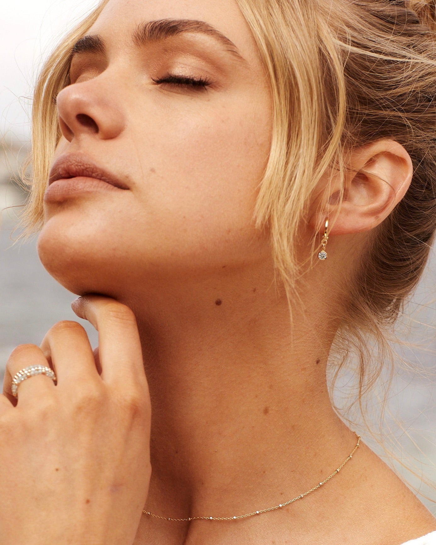 Close-up of a woman wearing gold jewelry including earrings, necklace, and ring.