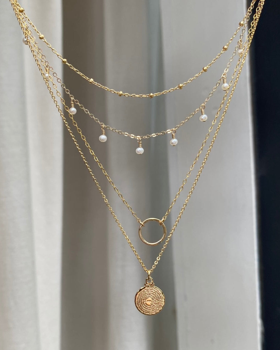 Four fine gold necklaces, one featuring pearl drops suspended in front of  a neutral background