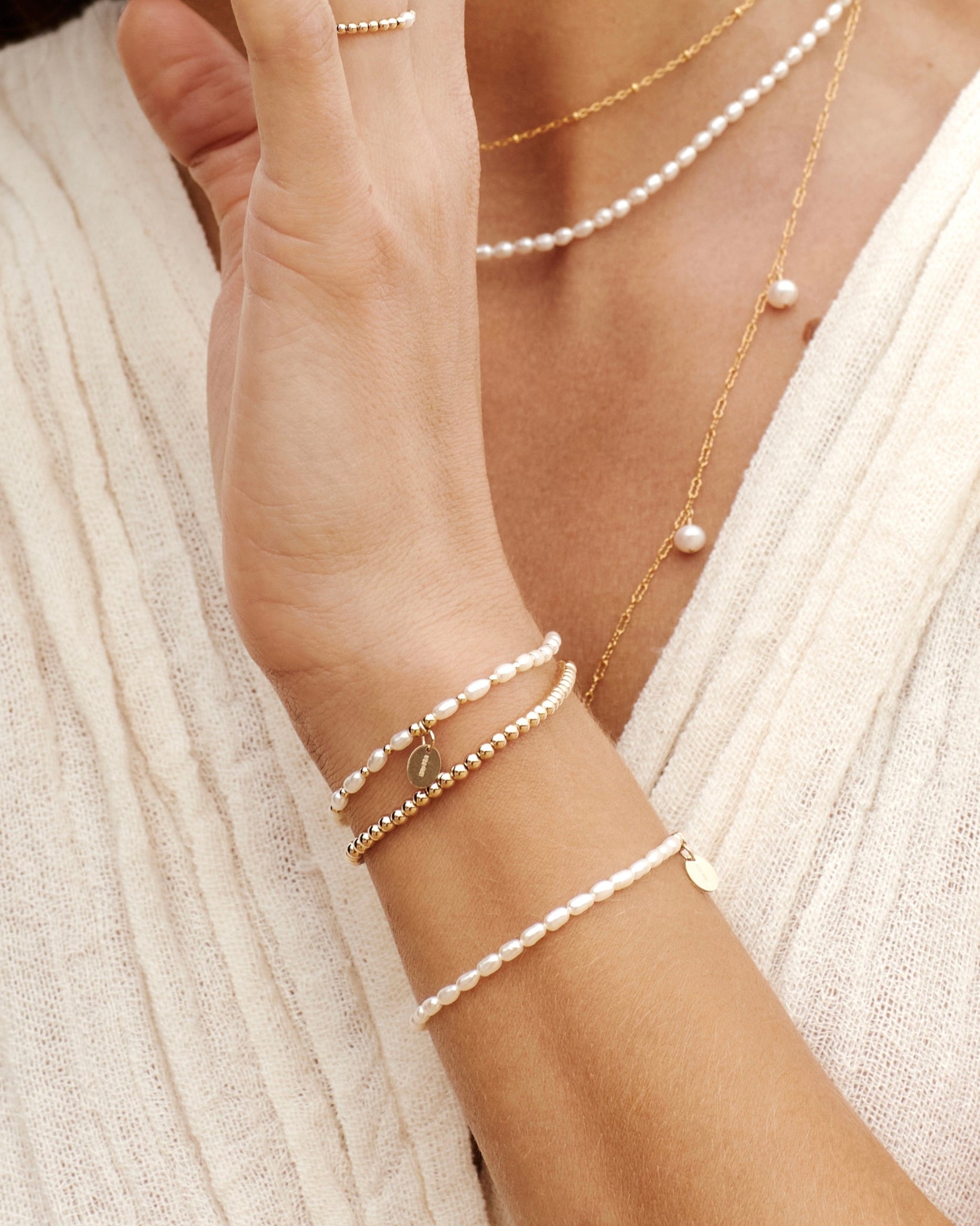 Close up of a woman wearing gold pearl jewellery including bracelets, rings and necklaces