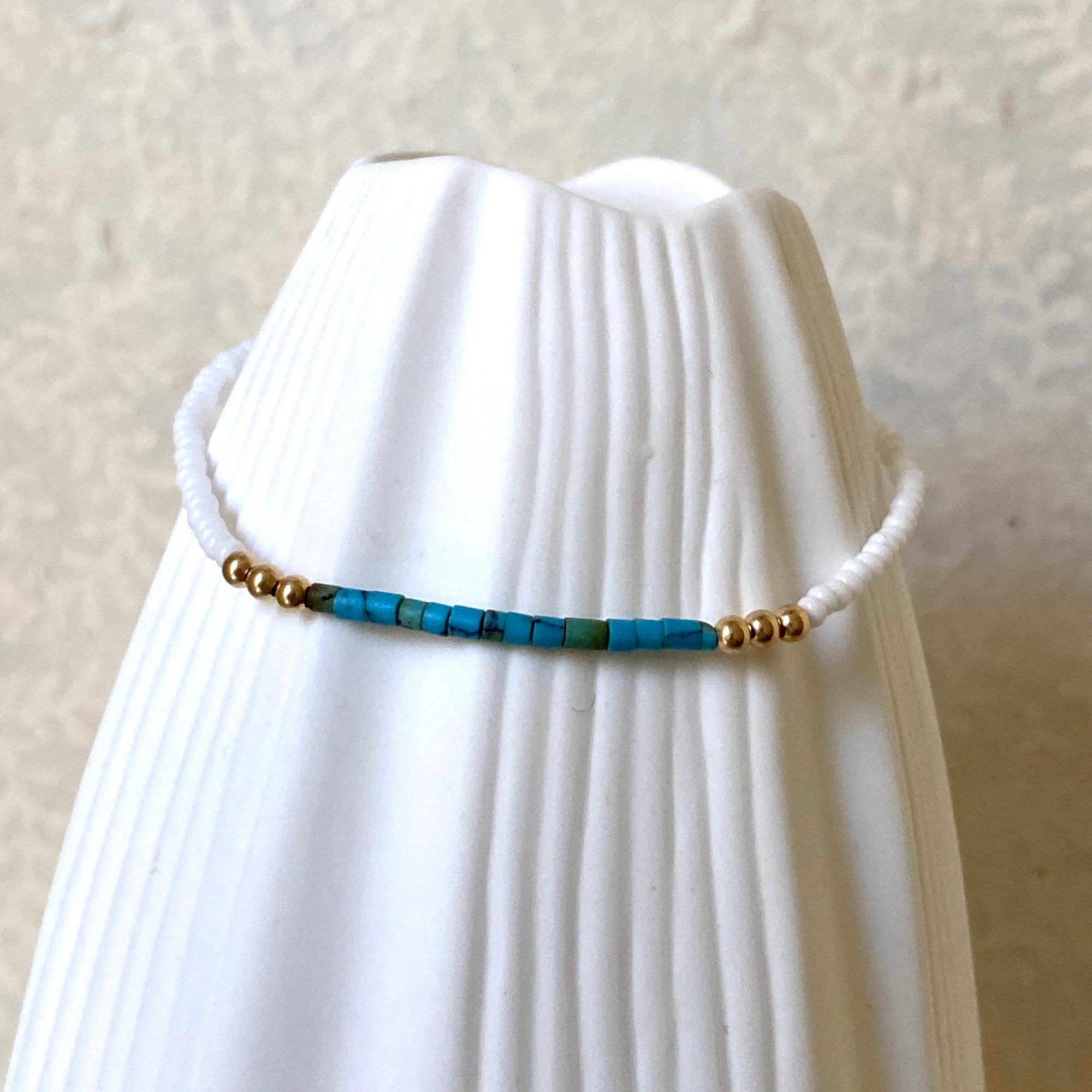 Turquoise, white and gold beaded bracelet  displayed on a white vase
