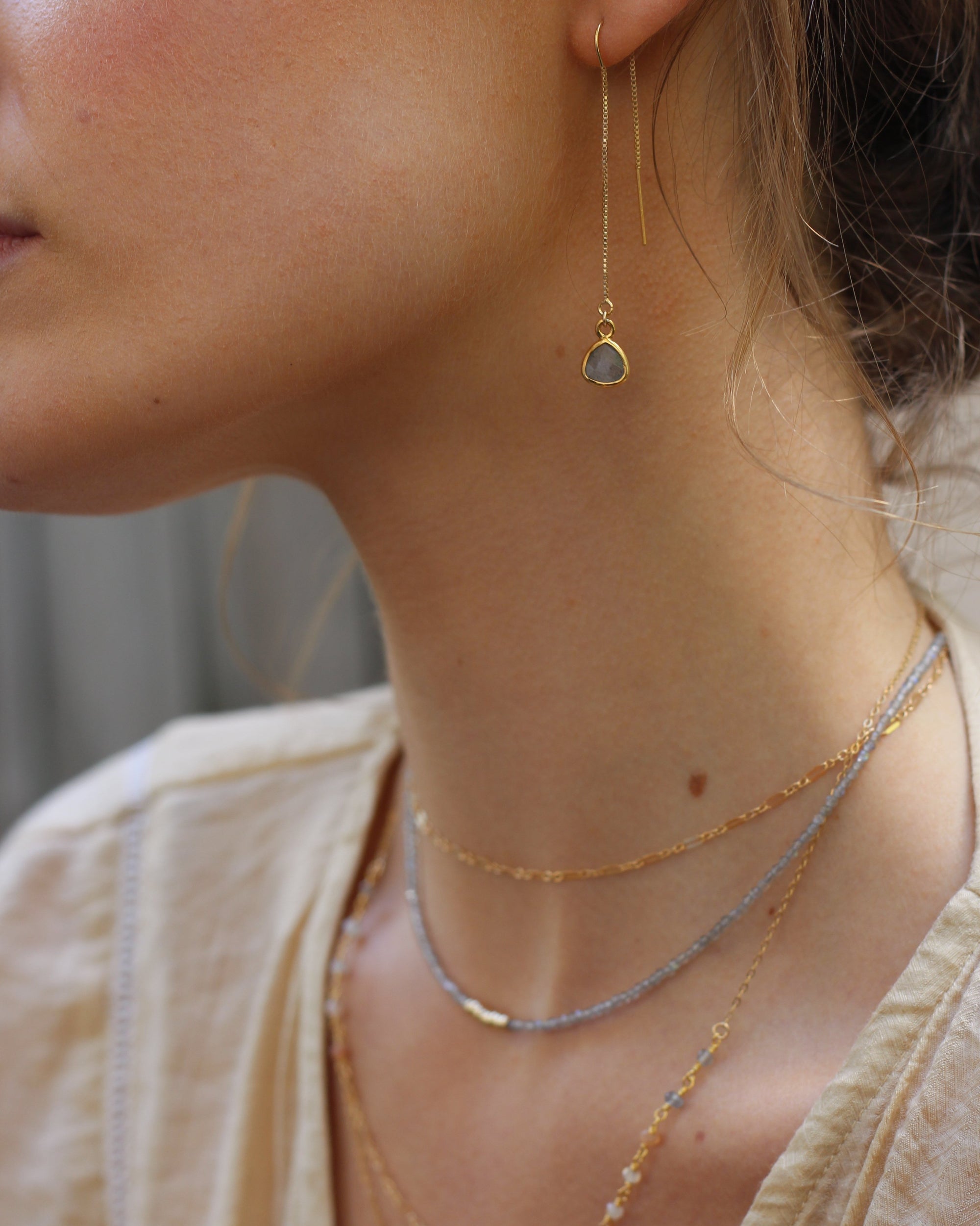 Close-up of a person wearing a delicate gold labradorite gemstone necklace and thread earrings